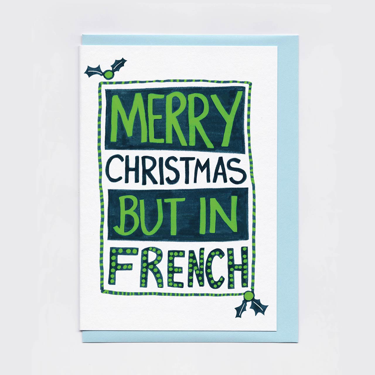 Merry Christmas but in French - white card, green and blue text, sitting on top of a pale blue A6 envelope.