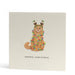 Square Christmas card featuring a cute orange cat wrapped in fairy lights. The words Merry Christmas are handwritten underneath. The cat is also wearing Christmas pudding deeley boppers.