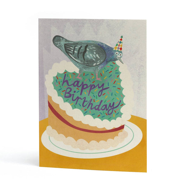 A cute birthday card featuring an illustration of a pigeon wearing a party hat perched on top of a birthday cake with the words 'Happy Birthday' written across it.
