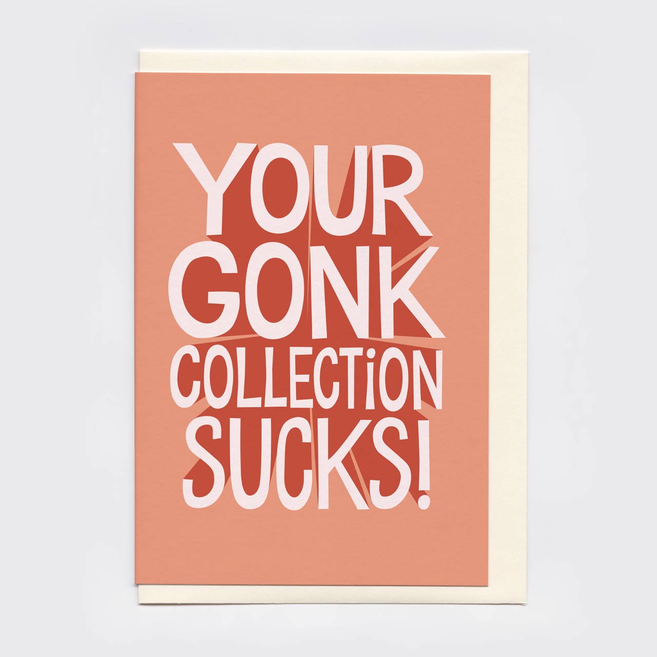 A rectangular greeting card with a peach-pink front and cream envelope. On the card is printed, in bold white text, 'YOUR GONK COLLECTION SUCKS!'