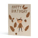 An A6 greeting card with a warm beige background, featuring the words 'HAPPY BIRTHDAY' in brown lettering, surrounded by illustrated brown oak leaves, acorns, and a cute cartoon child in a brown animal-ears outfit.