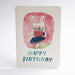 An A6 birthday card with rounded corners, featuring a hand-drawn illustration of a white rabbit holding a cake inside a pink oval, with the words 'HAPPY BIRTHDAY' in teal at the bottom.