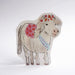 A die-cut greeting card featuring a hand-drawn illustration of a cream coloured pony with red and pink floral accents on its mane and back, wearing a blue 'HAPPY BIRTHDAY' ribbon, set against a plain light grey background.