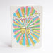 An A6 congratulations card with rounded corners, featuring a colourful burst design in pastel pink, blue, green, and yellow with two clinking champagne glasses and the word 'CONGRATULATIONS' on a banner, shown against a white background.