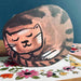 A die-cut card featuring a sleeping cat with a brown and black spotted fur pattern, resting on a white floral envelope set against a dark blue background.