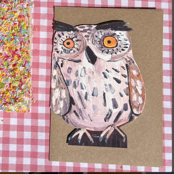 A die cut card featuring a hand-painted Little Owl, sitting on a brown kraft envelope, displayed on a gingham tablecloth next to a bag of rainbow sprinkles.