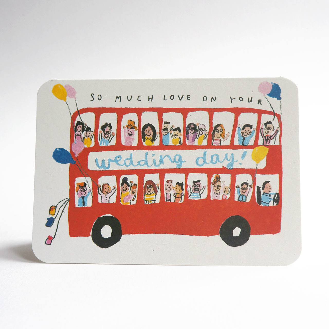 An A6 greeting card, tent fold, landscape, featuring a hand-drawn red double-decker bus with illustrated passengers and balloons, with the text 'SO MUCH LOVE ON YOUR wedding day!' across the front, photographed on a white background.