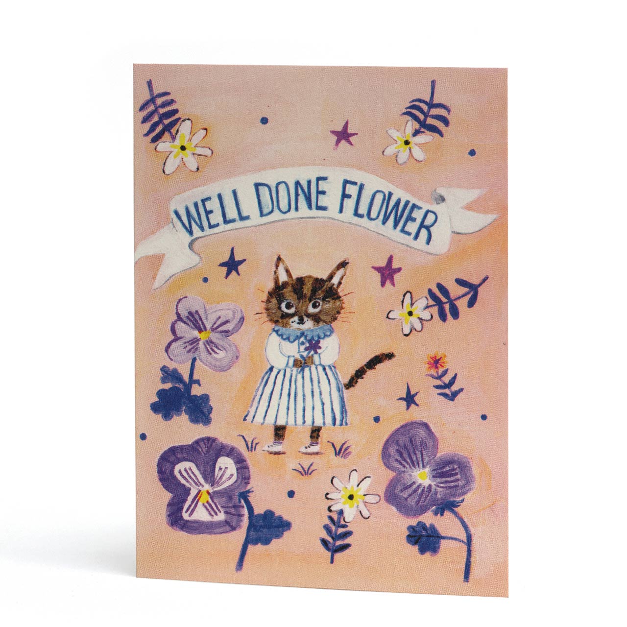 An A6 congratulations card featuring a whimsical illustration of a tabby cat in a blue-and-white dress surrounded by purple flowers and small stars, with a banner reading 'WELL DONE FLOWER' on a peach background.