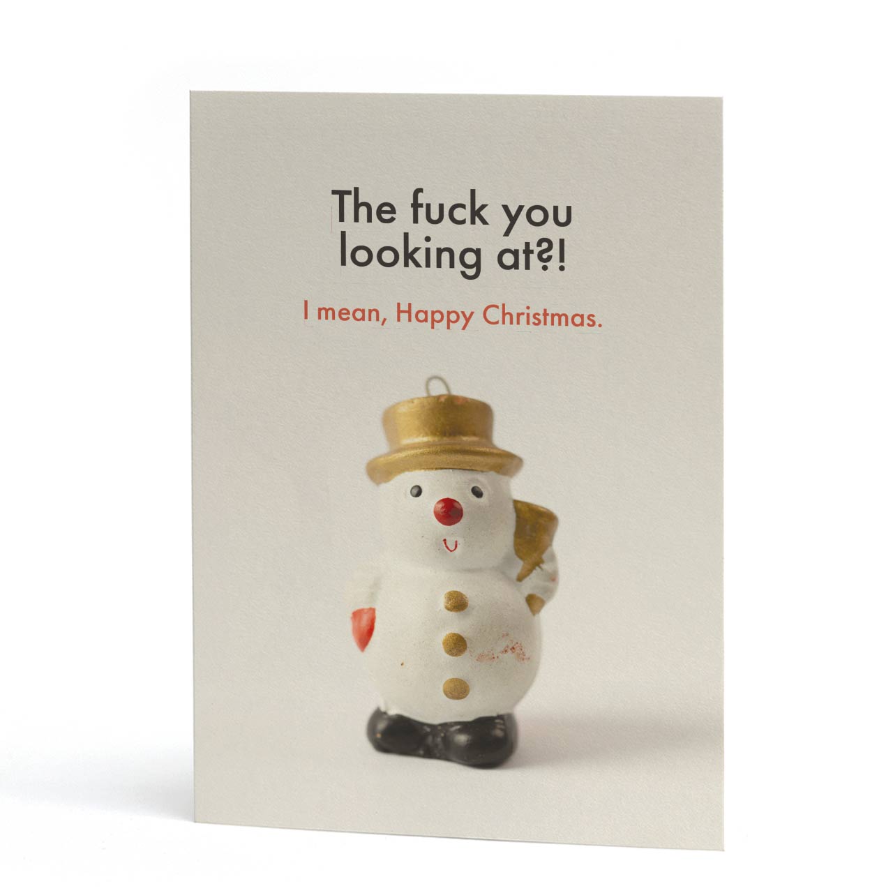 An A6, sweary, quirky Christmas card with a small snowman ornament on the front. The card has a light cream background and the snowman is saying, "The fuck you looking at?! I mean, Happy Christmas."