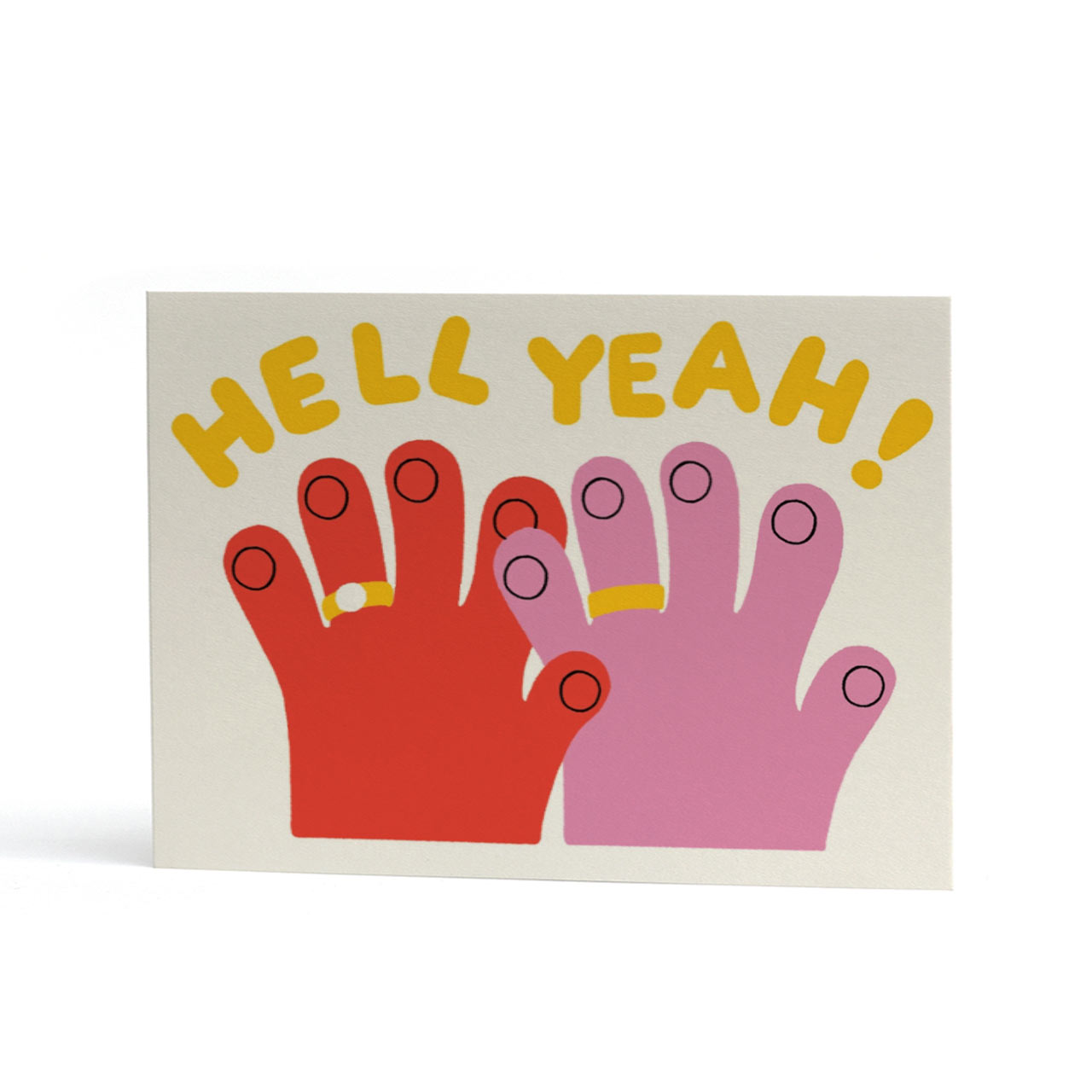 A landscape A6 greeting card with a white background featuring two stylised hands, one red and one pink, each with rings on their fingers, beneath the yellow text 'HELL YEAH!'.