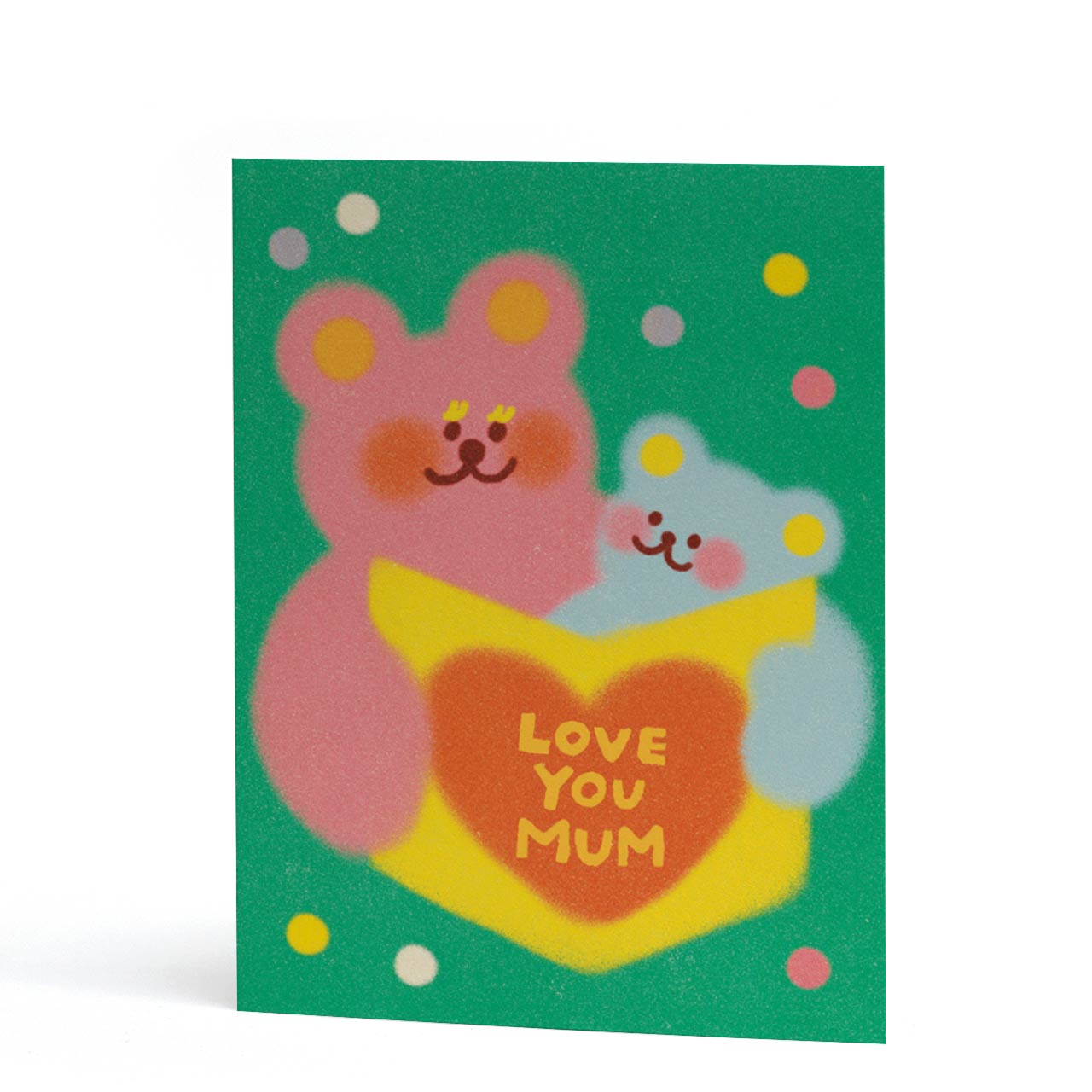 A6 Card for Mum with a green background featuring two cartoon teddy bears holding a yellow heart-shaped book that says 'LOVE YOU MUM' in yellow letters. The card is photographed standing upright against a clean white background.