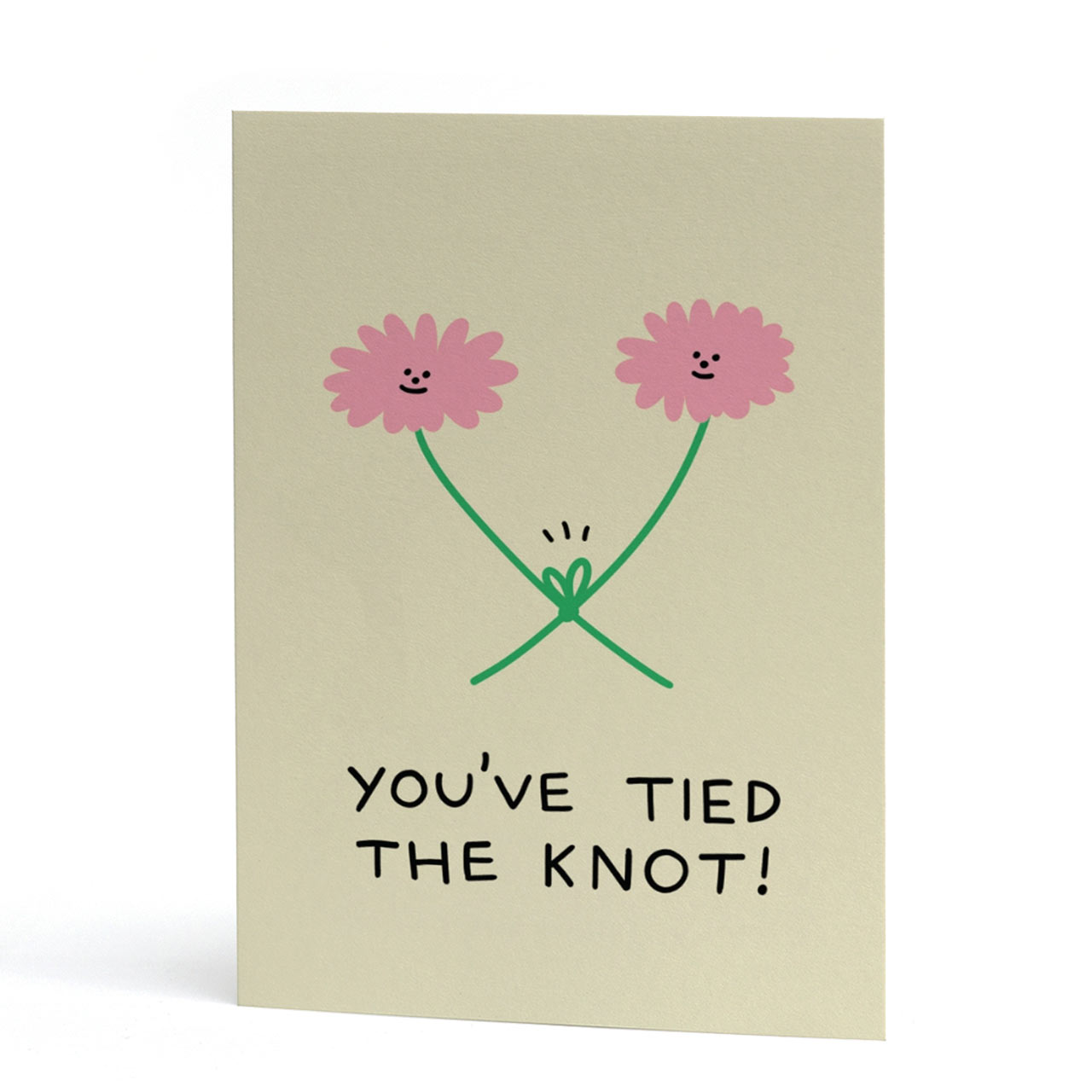 An A6 greeting card with a light beige background, featuring a hand-drawn illustration of two smiling pink flowers with green stems tied together, and the text 'YOU'VE TIED THE KNOT!' in black below.